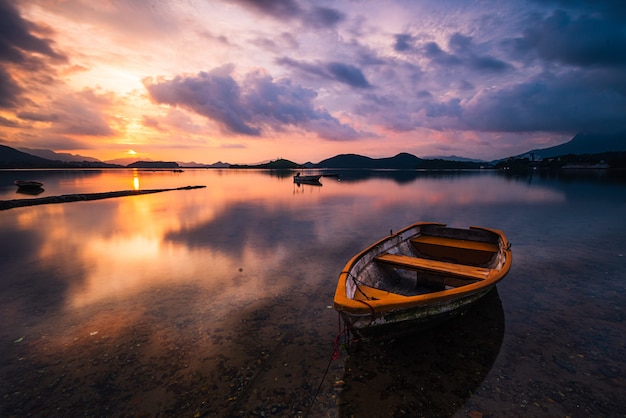 Free Photo beautiful shot of a small lake with a wooden rowboat in focus and breathtaking clouds in the sky
