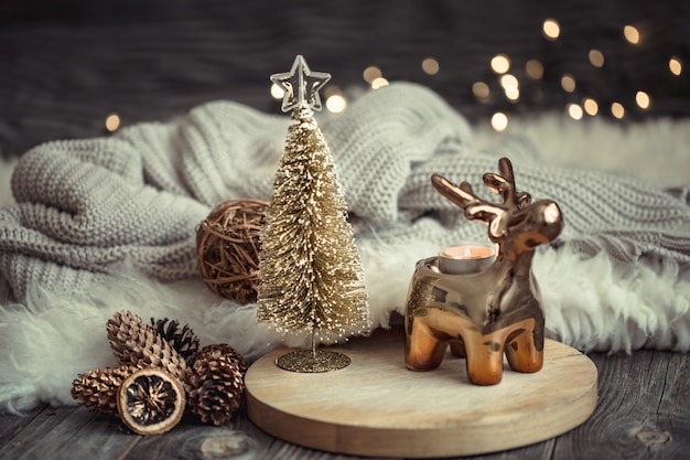 Free Photo christmas festive wall with toy deer with a gift box and christmas tree, blurred wall with golden lights on wooden deck table
