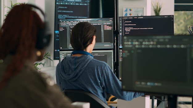 Free Photo database programer writing code on terminal window using multiple monitors in it agency office. system software developer typing database information, computing big data script.
