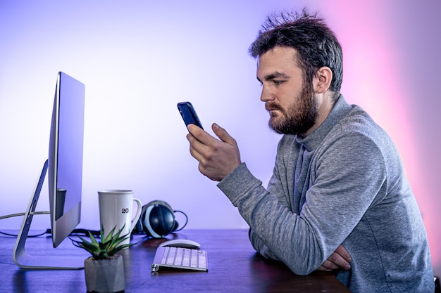 Free Photo a man sits in front of a computer uses a smartphone workplace