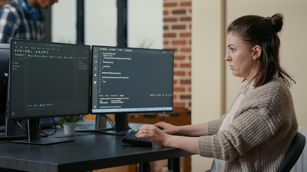 Free Photo portrait of focused programer writing code looking at multiple computer screens displaying programming language algorithm. software developer coding while colleagues doing teamwork in background.