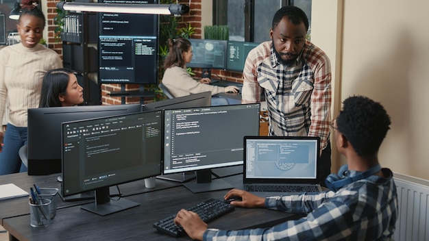 Free Photo programer sitting at desk with multiple screens running code talking with colleague about artificial intelligence algorithm. software developers doing innovative artificial intelligence project.