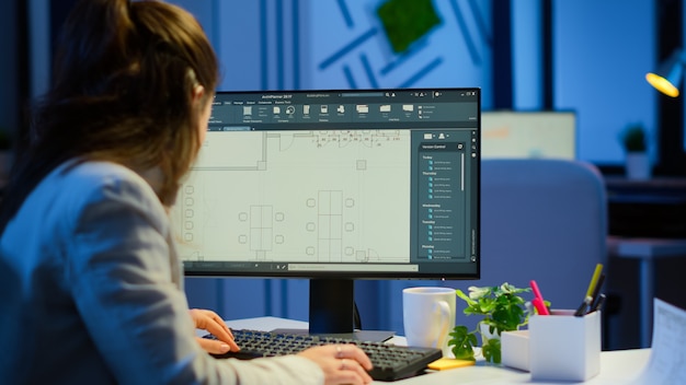 Free Photo over the shoulder shot of engineer working with architectural plans, cad software on desktop computer. designer using arhitecture blueprints of buildings working overtime, creating and studying