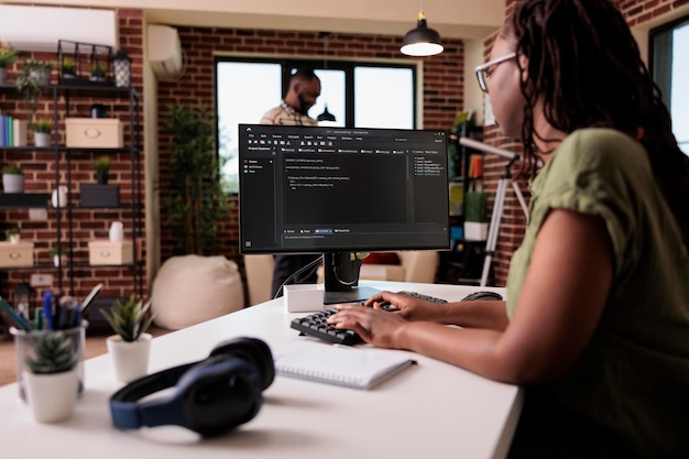 Free Photo woman coder developing software for freelance project working remote from home while boyfriend is relaxing. african american programmer writing source code looking for errors while debugging.