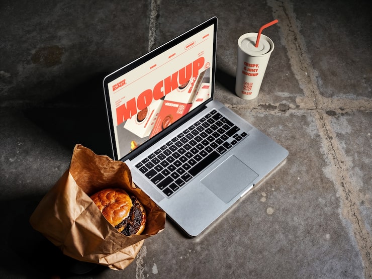 Free PSD laptop mockup with burger, drink, and food packaging.