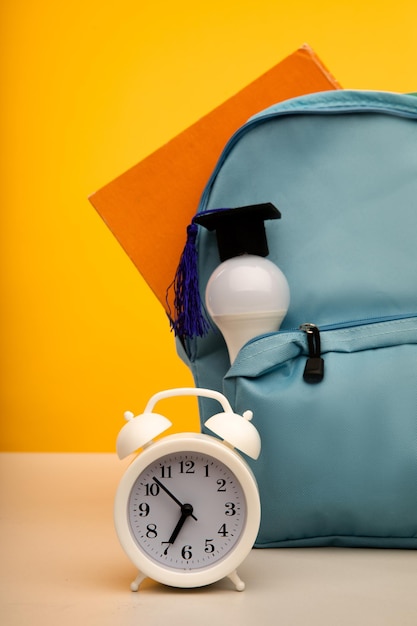 Photo bright backpack alarm clock and bulb education concept vertical image