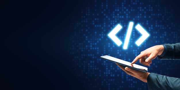 Photo close up of businessman hand pointing at tablet with glowing programming code on blue binary coding background with mock up place program and software development concept