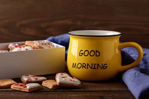 Photo closeup cheerful morning with yellow cup of coffee or tea with box of cookies hearts on wooden background, good morning concept
