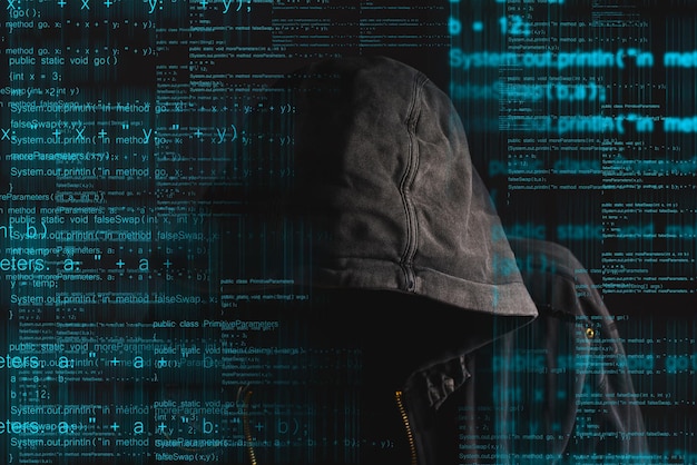 Photo faceless hooded anonymous computer hacker with programming code from monitor deep web hacking and ransomware concept