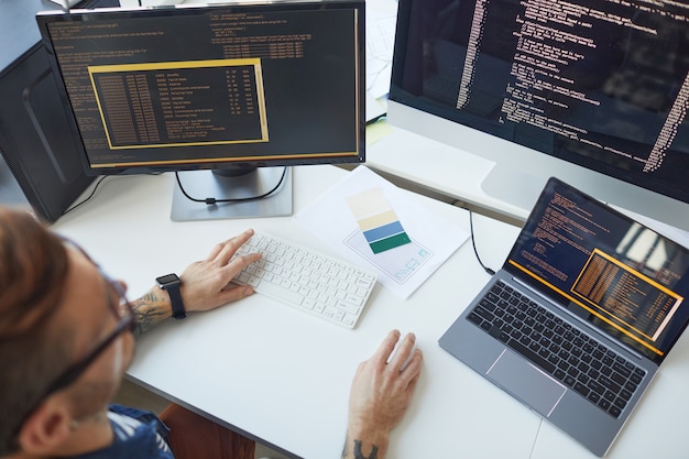 Photo high angle view at male programmer writing code while using multiple computers in it developers office , copy space
