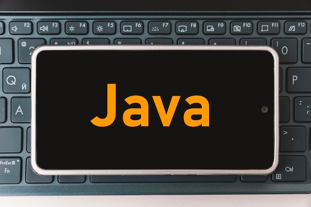 Photo java programming language for mobile development concept smartphone on the laptop keyboard the programmer workplace inscription java on mobile phone screen
