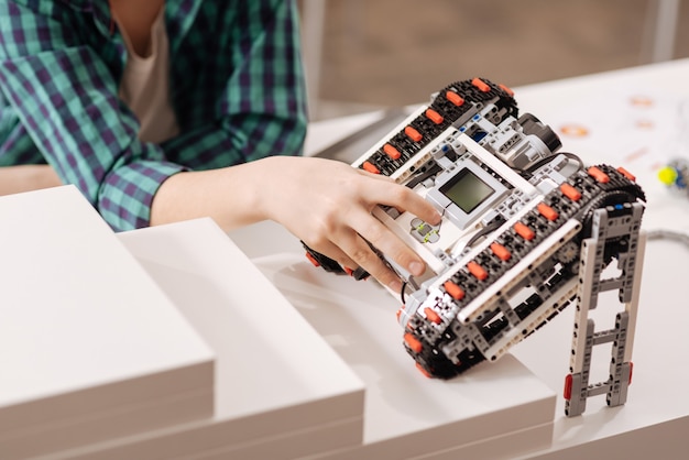 Photo modernized device. skilled smart young boy sitting in the classroom while expressing gladness and programming robot