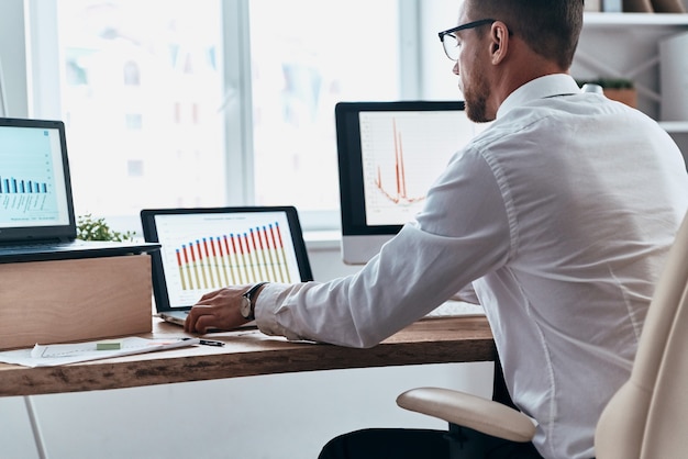 Photo really busy. young businessman in formalwear analyzing data using computer while sitting in the office