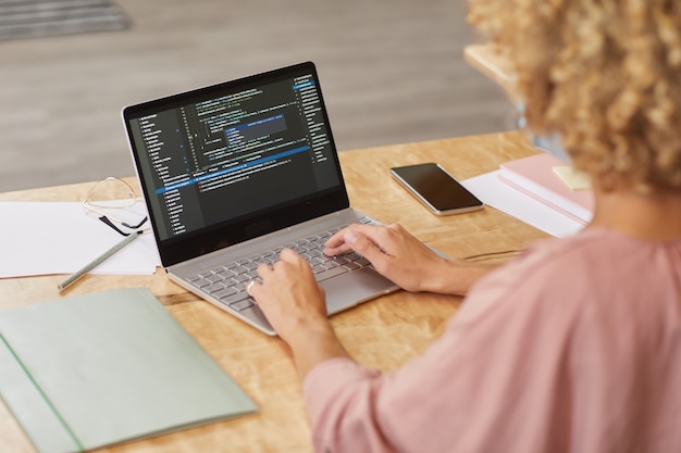 Photo rear view of programmer sitting at the table and typing on laptop computer she testing new computer program