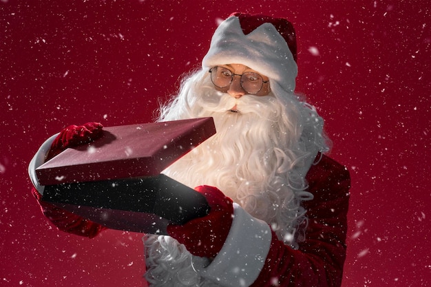 Photo santa claus holding and opening gift box isolated on red background holiday new year magic