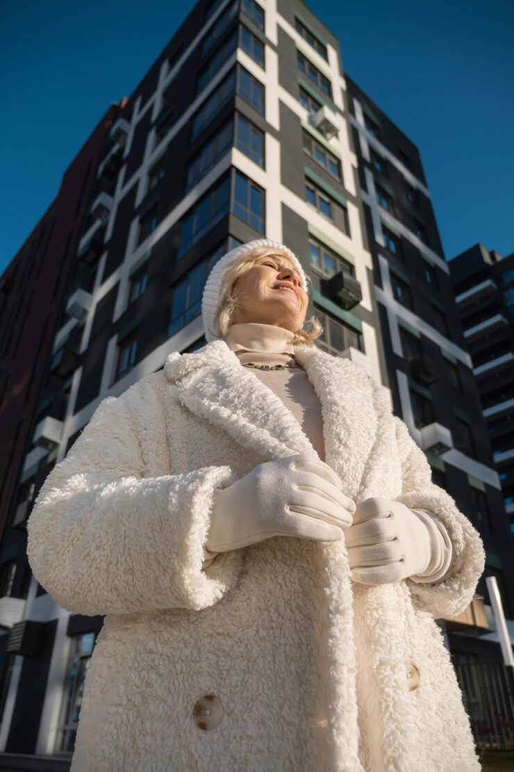 Smiling senior woman wearing winter clothes standing near modern building