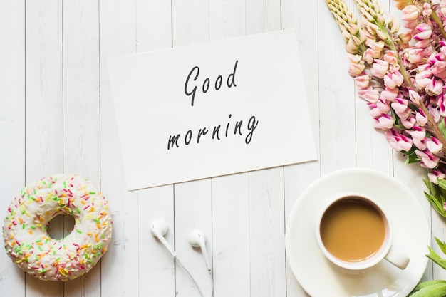 Photo still life with a cup of coffee and lupine flowers donut on a light wooden table. copy space