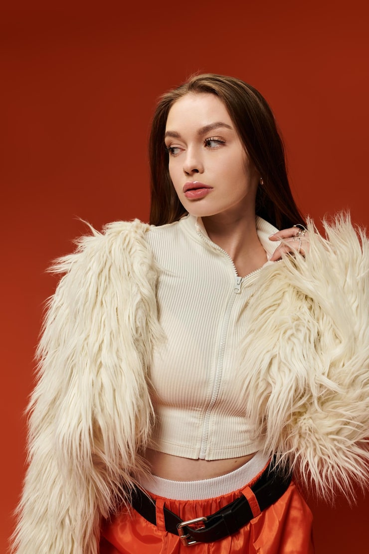 Vibrant stylish woman poses confidently with a fashionable outfit against a bright orange background