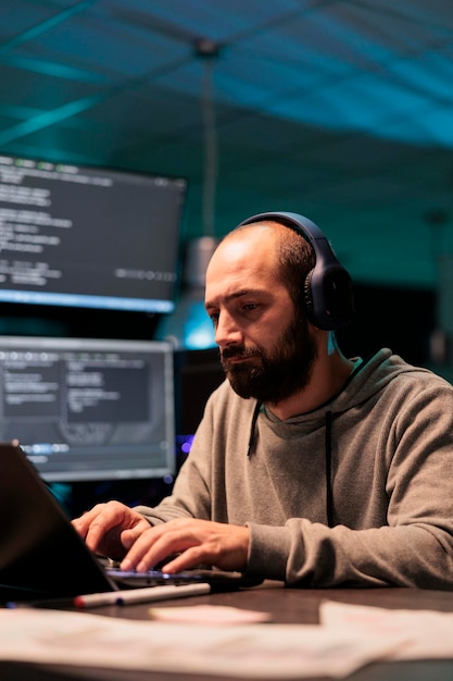 Photo young app developer writing code and listening to music on headphones, using artificial intelligence script to program big data on laptop. programming server on terminal window.